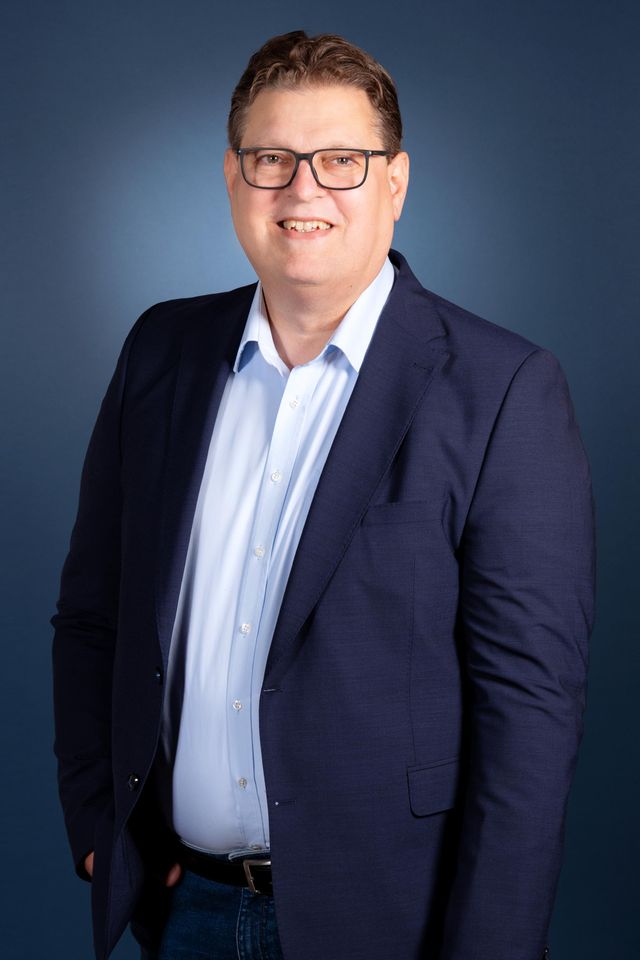 Smiling businessman in dark blazet und weißem Hemd mit Brille, professionelles Porträt.
